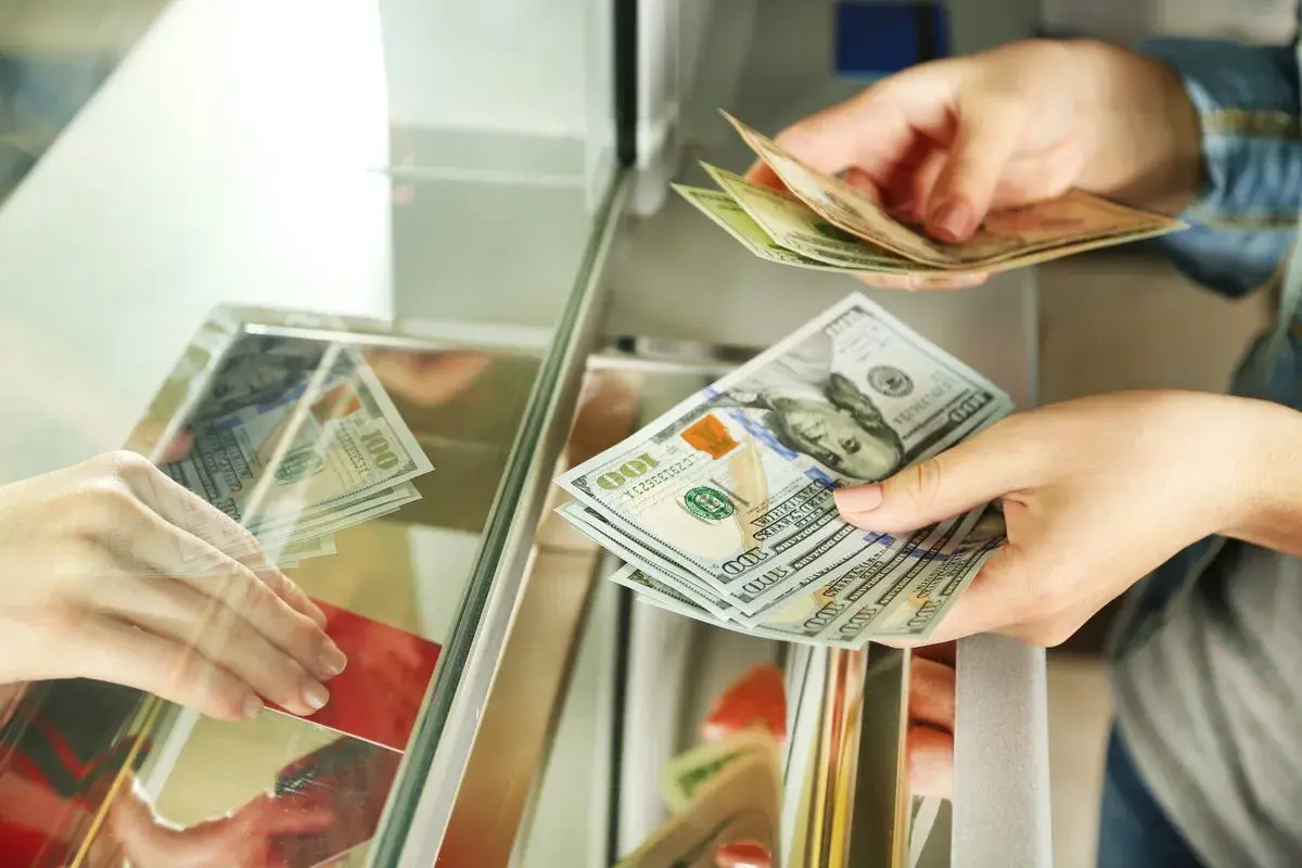 Wymiana pieniędzy w Tunezji: euro czy dolary? Dłonie przekazują sobie banknoty 100 dolarów.