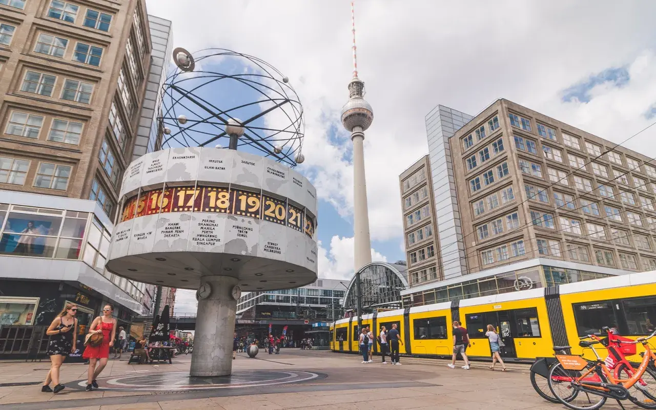 Wieża telewizyjna Berlin góruje nad placem z zegarem światowym i żółtym tramwajem.