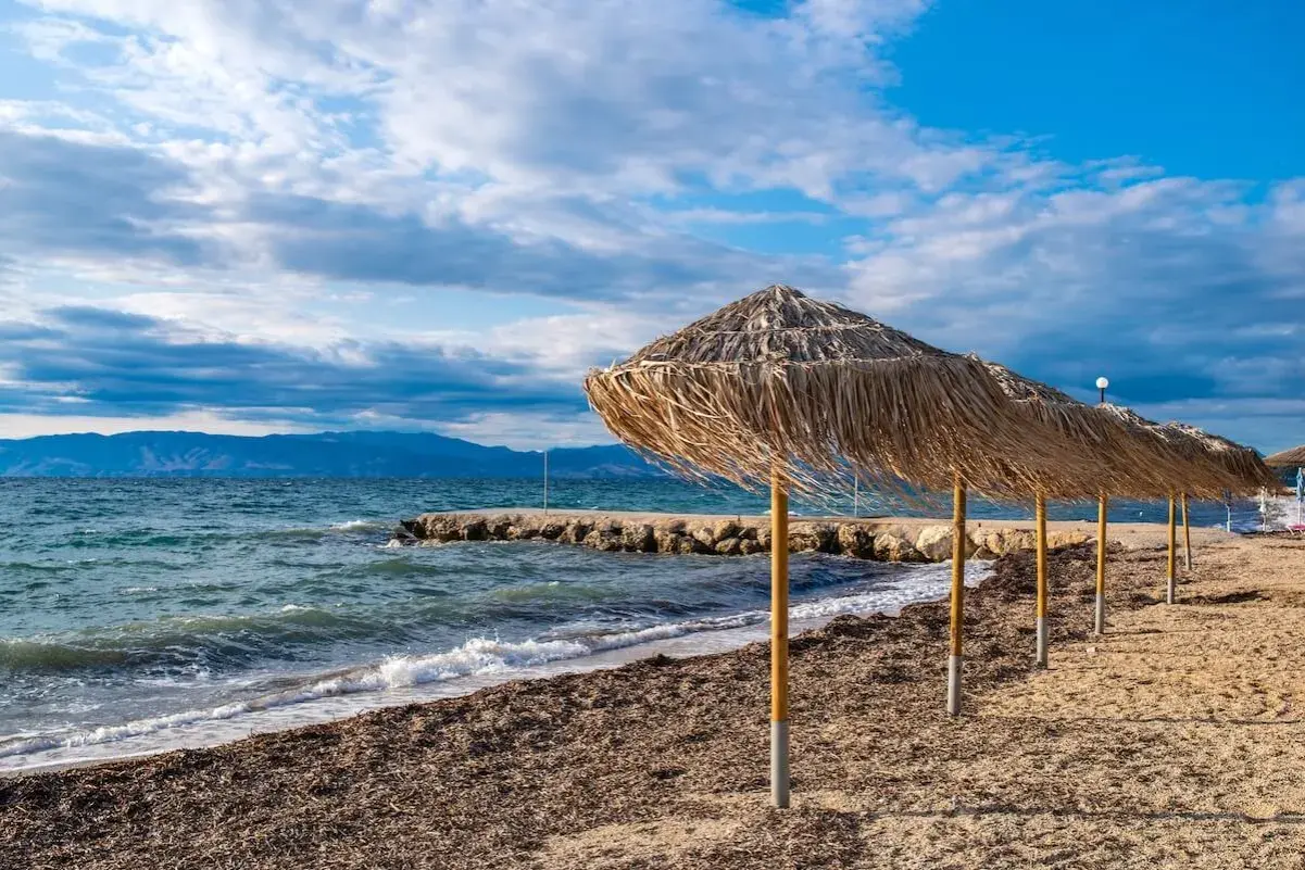 Słomiane parasole na plaży Angela Beach Korfu, morze i góry w tle.