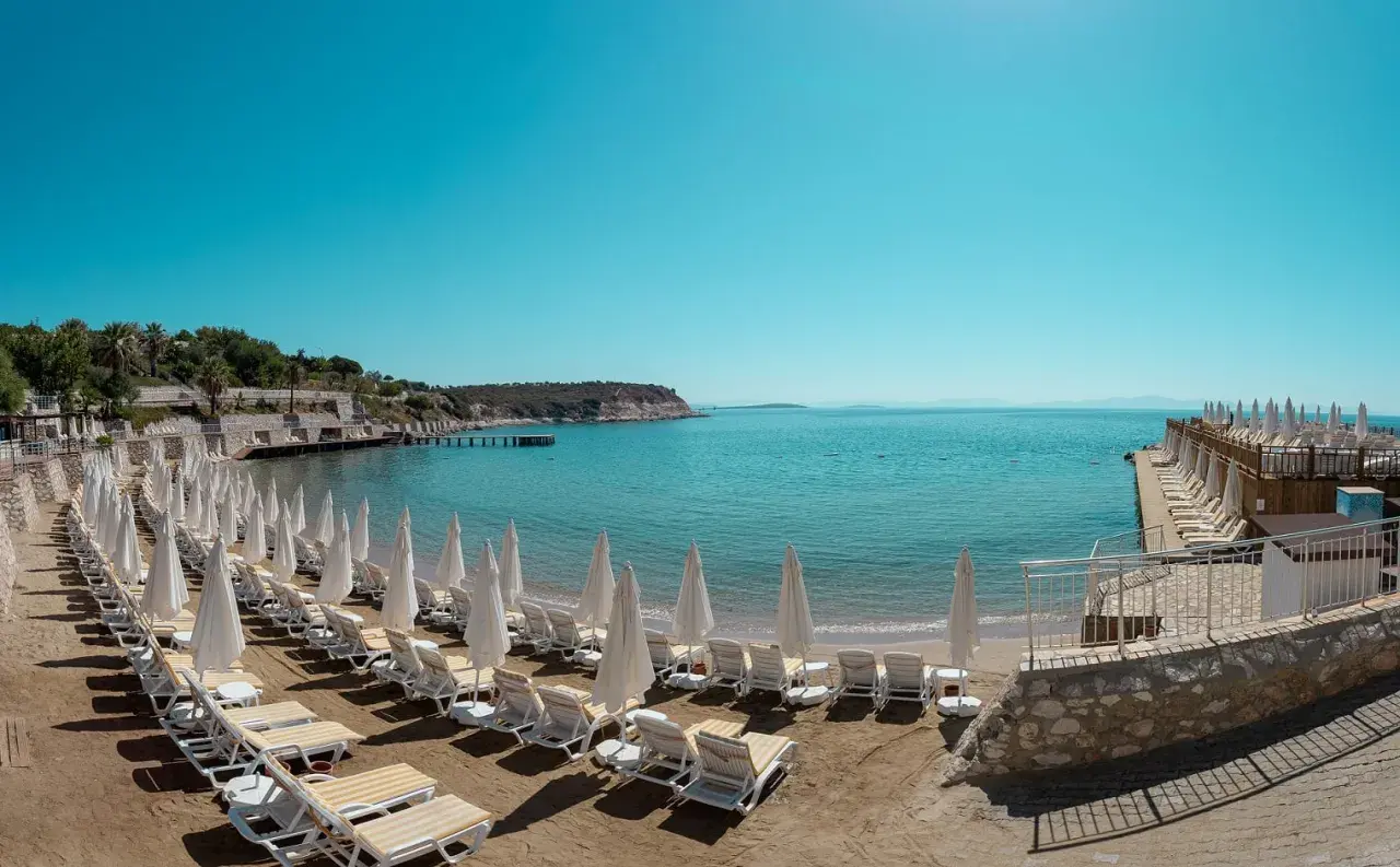 Plaża z rzędami leżaków i parasoli w Anadolu Hotels Didim Club. Błękitne morze i spokojne niebo zapraszają do relaksu.