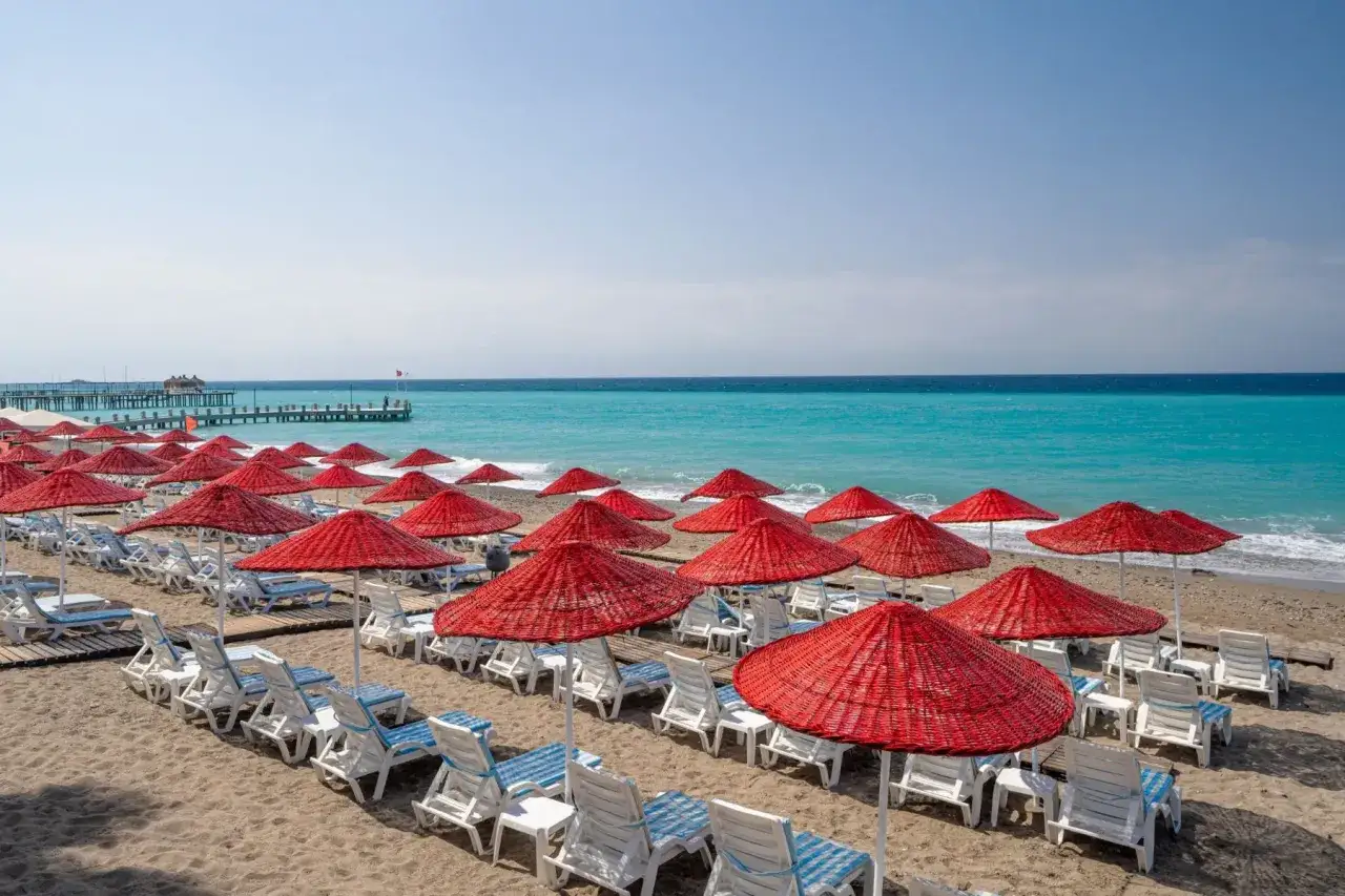 Plaża z rzędami leżaków i czerwonych parasoli, idealna na luksusowy wypoczynek w Okurcalar.