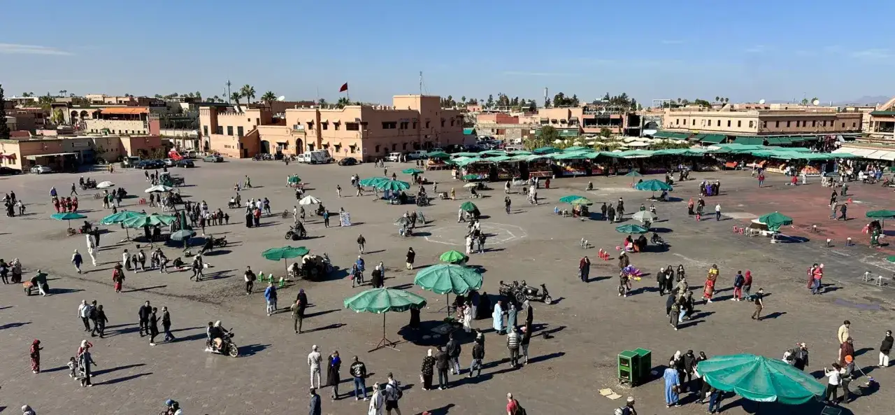 Tętniący życiem plac Dżamaa al-Fana w Marrakeszu. Ludzie spacerują, kupują na straganach, podziwiają architekturę. To serce miasta, które warto zobaczyć.