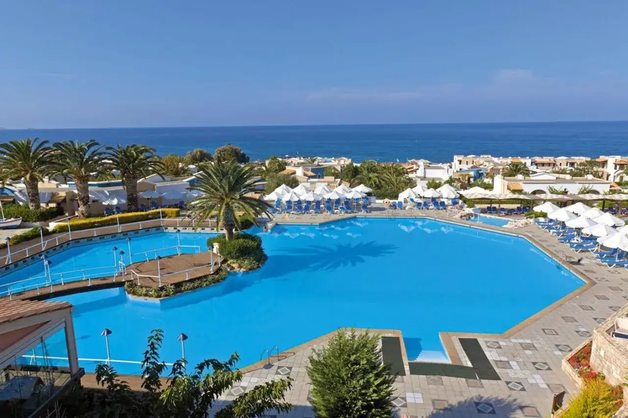 Luksusowy basen w Aldemar Knossos Royal, otoczony palmami i z widokiem na morze. Idealne miejsce na relaks.