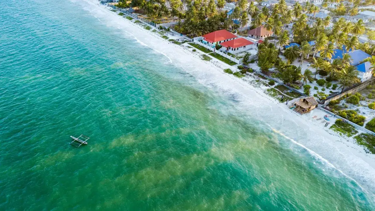Widok z lotu ptaka na plażę Zanzibaru z turkusową wodą, łodzią i domkami.