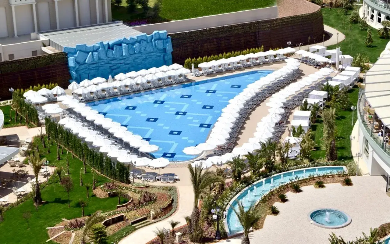 Lara, Delphin Imperial: rozległy basen z leżakami i parasolami, otoczony zielenią i architekturą hotelową.
