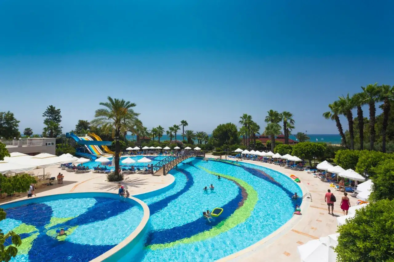 Słoneczny dzień w Side Star Resort. Dzieci bawią się w basenie z wodnymi zjeżdżalniami, dorośli odpoczywają pod palmami.