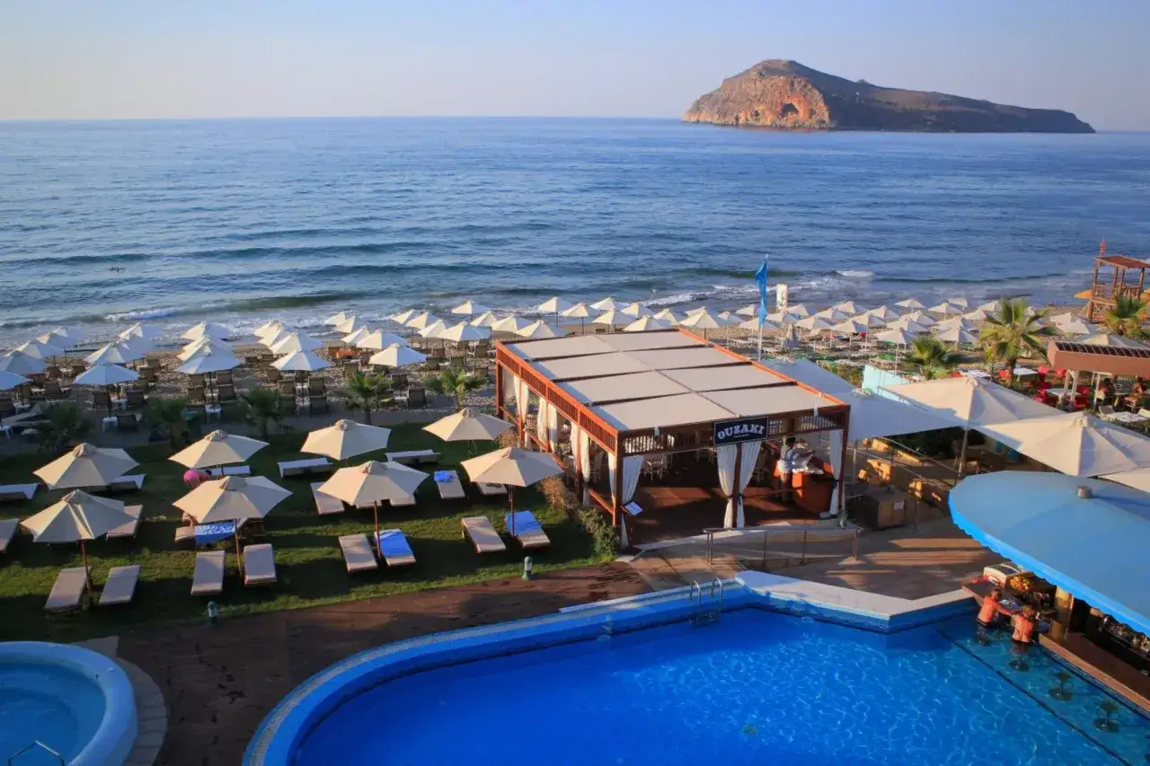 Widok na plażę z leżakami i parasolami, basen i bar przy hotelu Solimar White Pearl. W oddali widać wyspę.