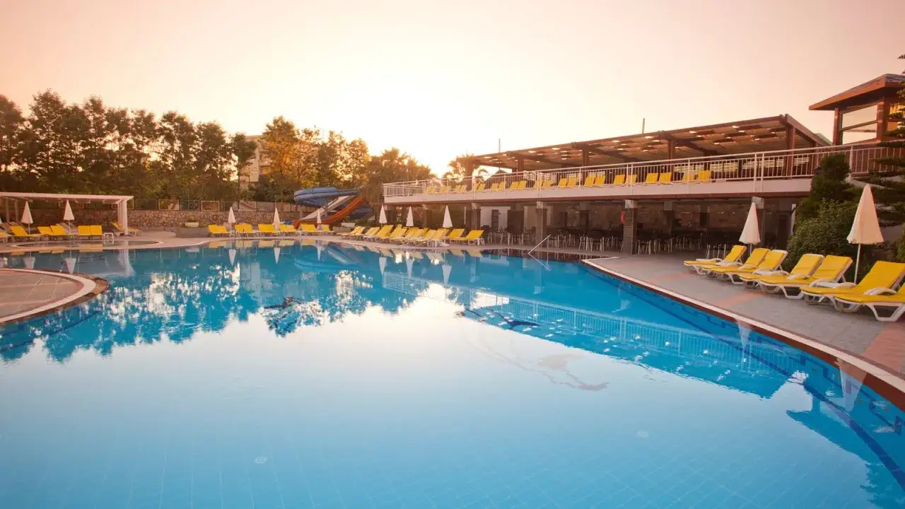 Basen w club mermaid village z leżakami i zjeżdżalniami wodnymi, otoczony drzewami, w ciepłym świetle zachodzącego słońca.