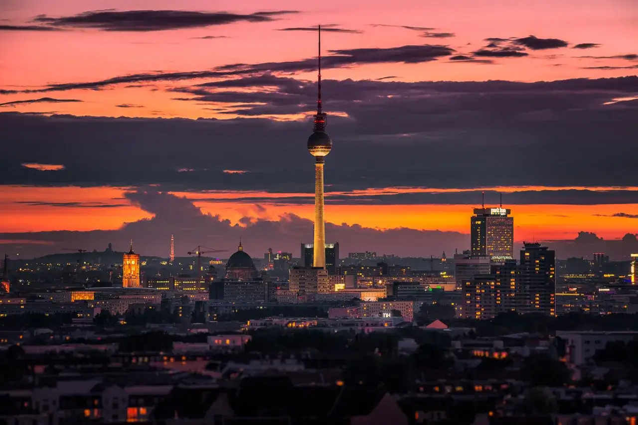 Wieża telewizyjna Berlin w zachodzącym słońcu, z kolorowym niebem i oświetlonymi budynkami.