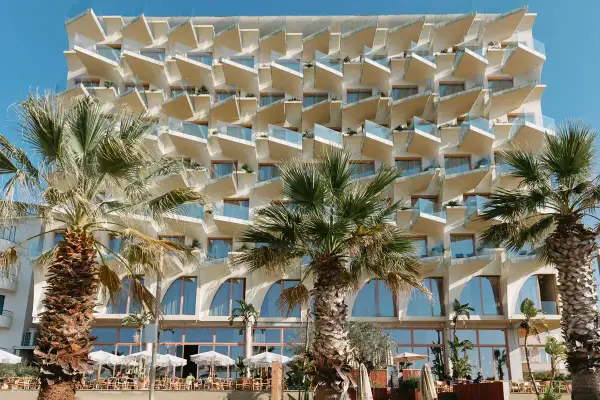 Nowoczesny hotel z białymi, geometrycznymi balkonami i palmami przed fasadą. Epidamn white sensation.