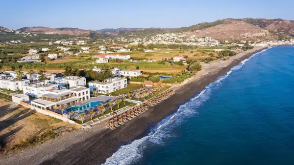 Hotel Solimar White Pearl, białe budynki z basenem i leżakami, rozciągają się wzdłuż ciemnej plaży i turkusowego morza.